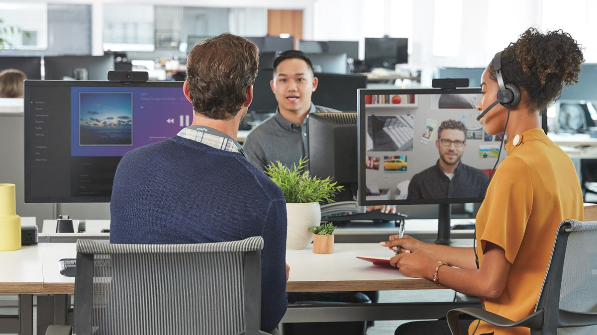 Office worker on a call in a Logitech Zone Wired headset while colleagues talk nearby