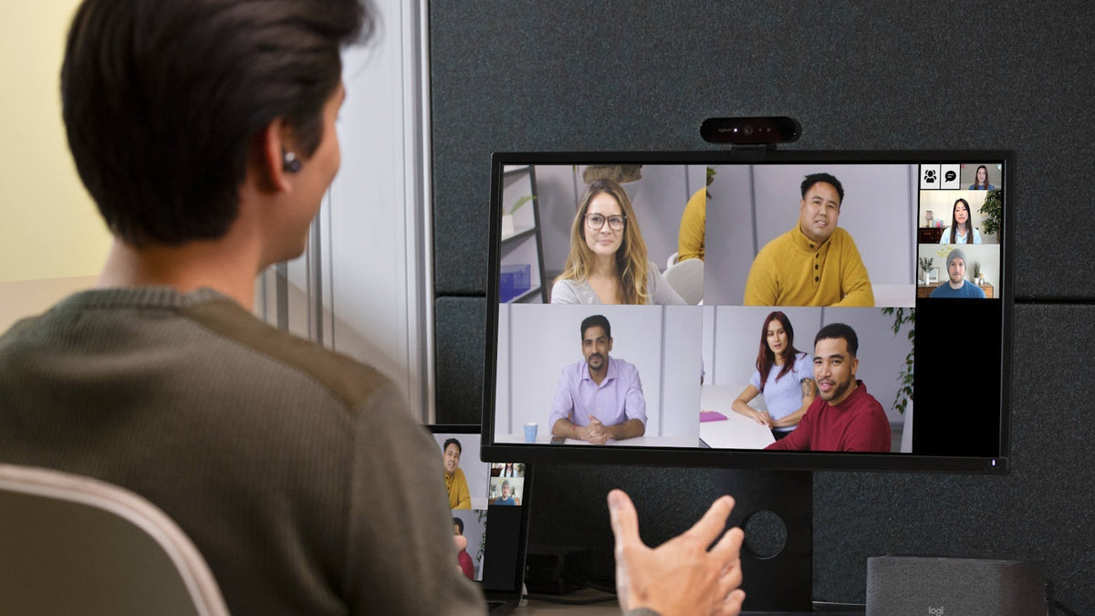 Person in a video meeting with remote colleagues shown on a display with a Logitech camera