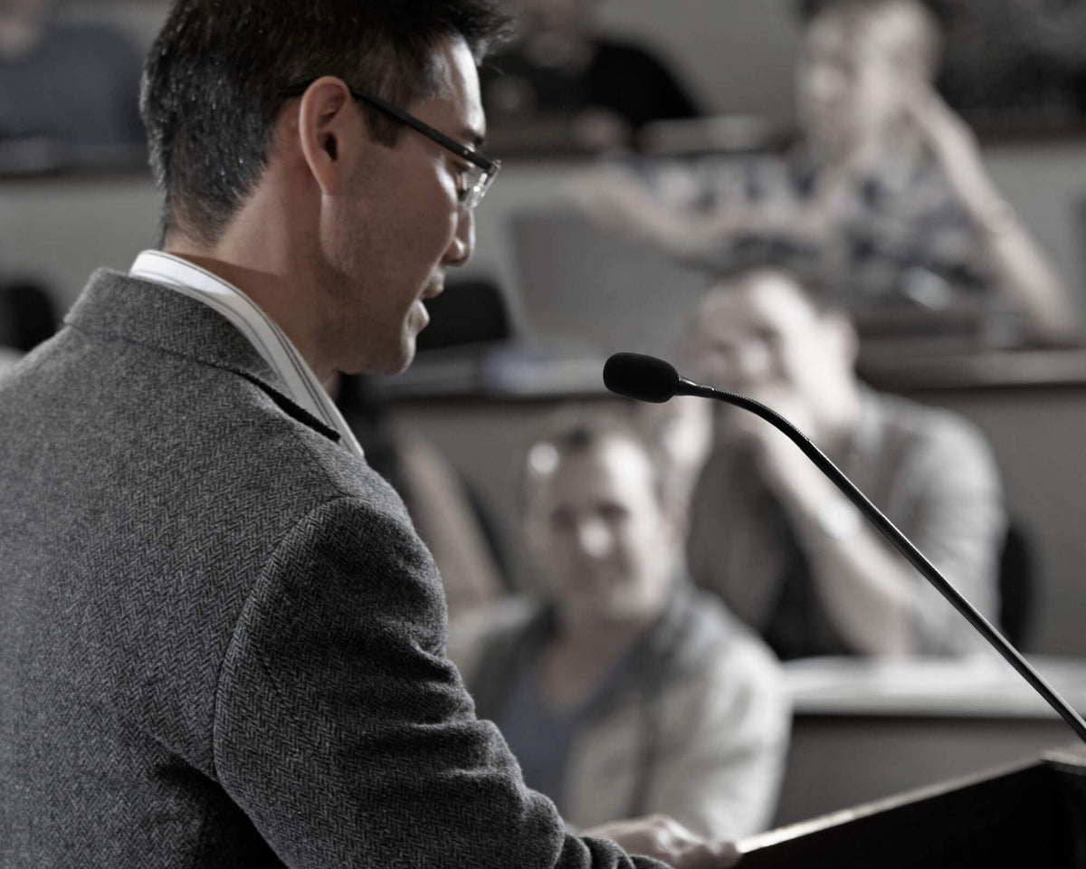 Lecturer speaking into a Shure gooseneck microphone at a lectern in a lecture hall