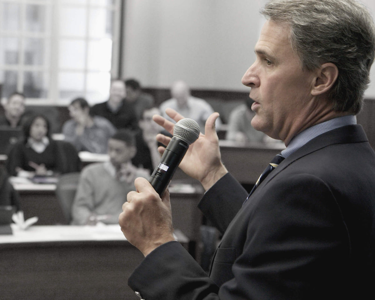 Presenter speaking into a Shure handheld wireless microphone in a training room